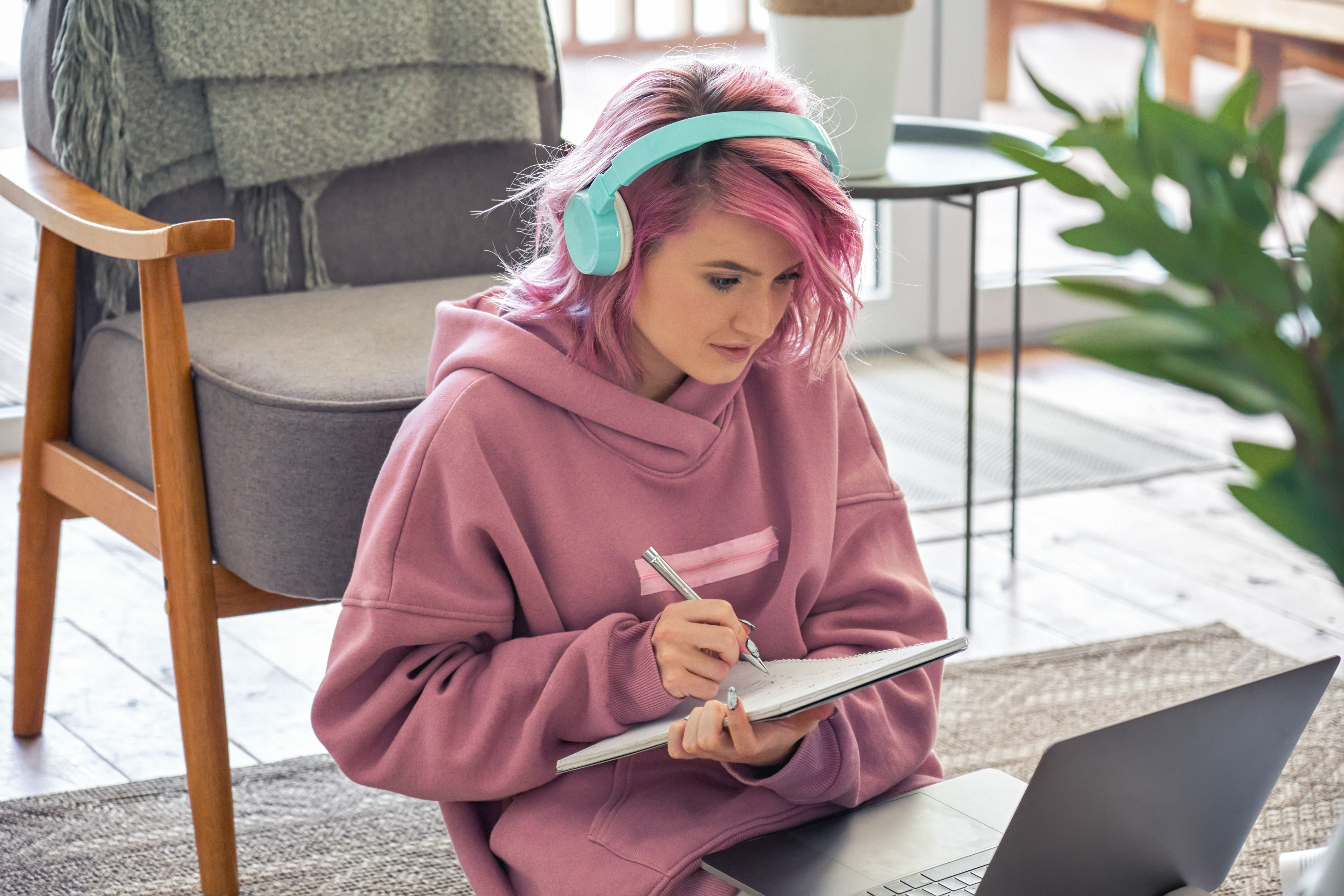girl with headphones on writing on notepad in front of laptop