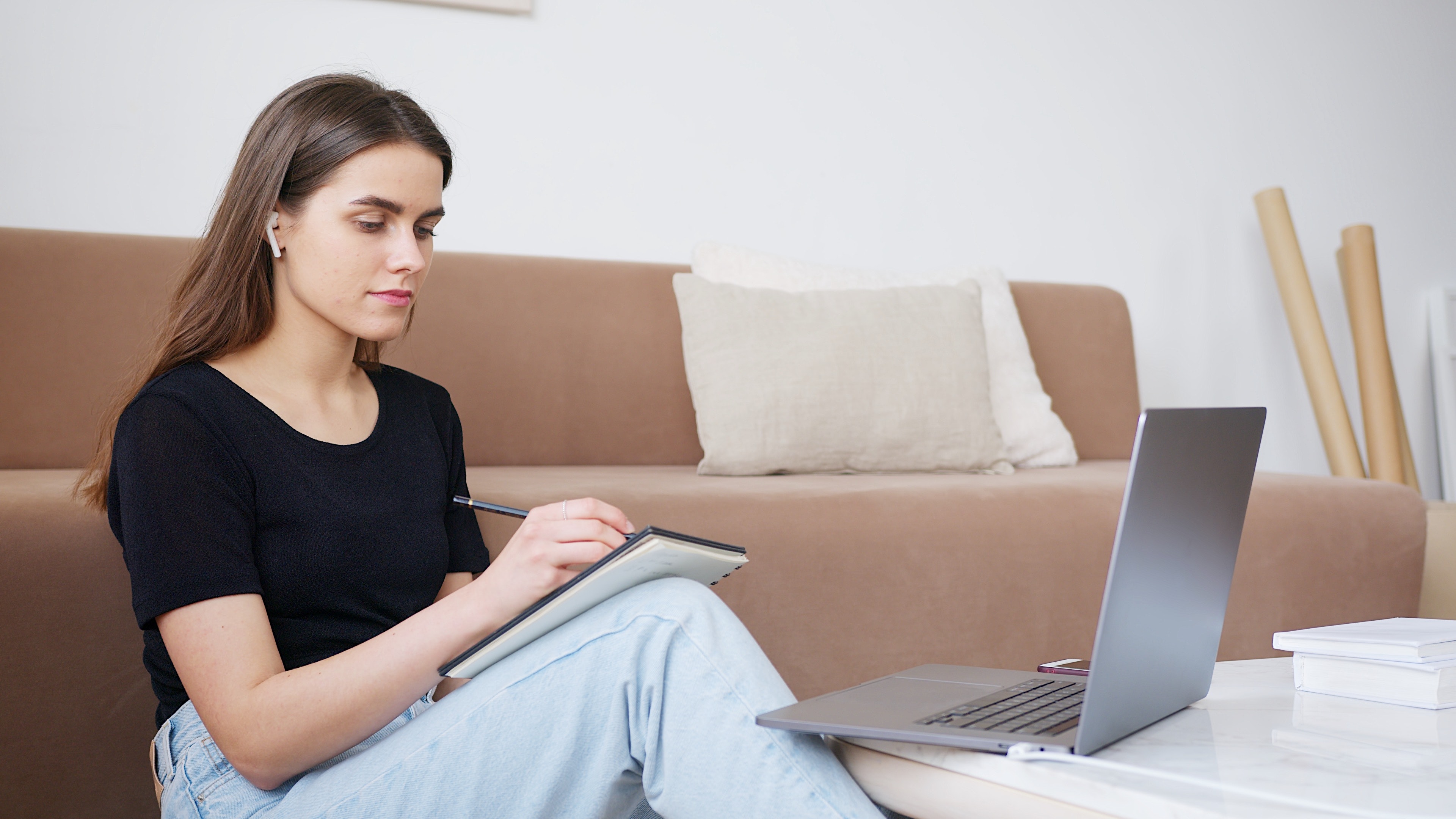 female writing in notebook in front of laptop